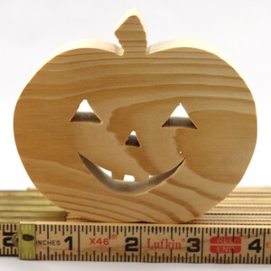 Handmade unpainted wooden Jack-o-Lantern cutout with carved triangular eyes, nose, smiling mouth, and stem, shown freestanding on a white background. Ready to paint for Halloween decoration.