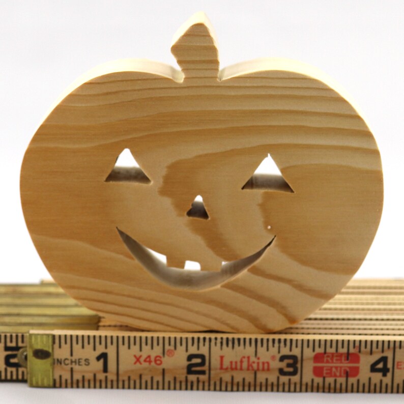Handmade unpainted wooden Jack-o-Lantern cutout with carved triangular eyes, nose, smiling mouth, and stem, shown freestanding on a white background. Ready to paint for Halloween decoration.