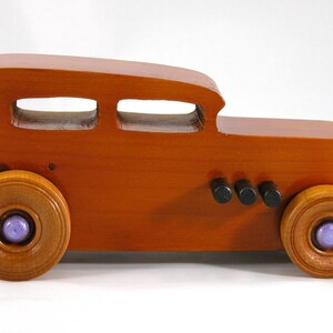 This is a handmade wooden toy car modeled after a Hot Rod 1932 Ford Sedan. It is made from wood, finished with multiple coats of amber shellac, and trimmed with black and metallic purple acrylic paint.