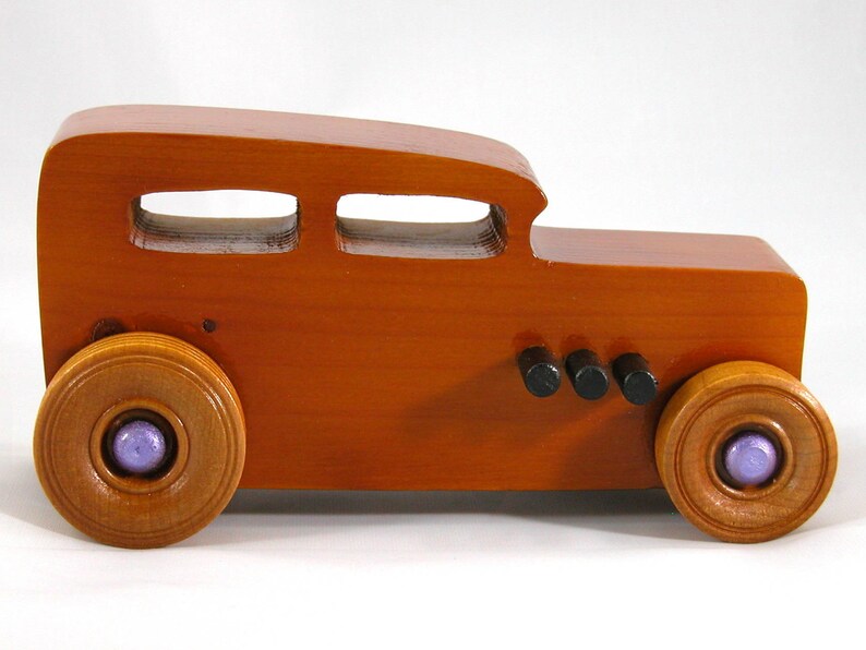 This is a handmade wooden toy car modeled after a Hot Rod 1932 Ford Sedan. It is made from wood, finished with multiple coats of amber shellac, and trimmed with black and metallic purple acrylic paint.