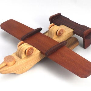 May include: A handcrafted wooden toy airplane with a biplane design. The wings and tail are a rich, dark brown, contrasting with the lighter natural wood of the fuselage and wheels. The propeller is also made of light wood.