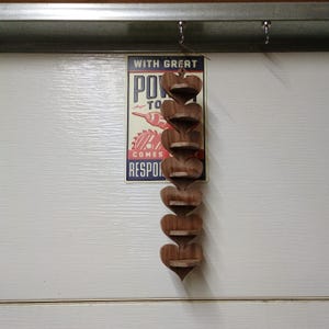 May include: A vertical wooden wall display featuring six connected heart-shaped shelves. Each heart has a small horizontal platform for storage. The unit is suspended by a thin string. Behind it is a rectangular sign with the text WITH GREAT POWER COMES GREAT RESPONSIBILITY.