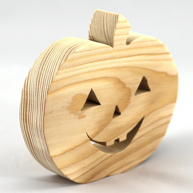 Handmade unpainted wooden Jack-o-Lantern cutout with carved triangular eyes, nose, smiling mouth, and stem, shown freestanding on a white background. Ready to paint for Halloween decoration.