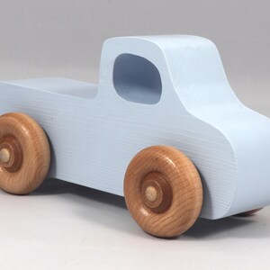 May include: A light blue wooden toy truck with natural wood wheels. The truck has a classic pickup design with a cab and a cargo bed. The wheels are round and made of light-colored wood. The toy is painted in a soft, pastel blue.