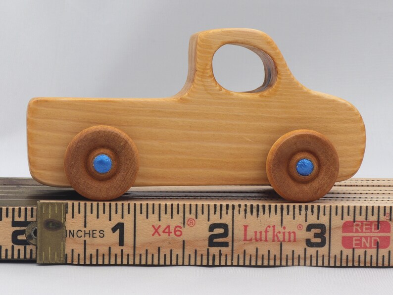 Wooden toy pickup truck from the Play Pal Collection at Odin's Toy Factory. Made from natural wood, finished with amber shellac, and accented with metallic sapphire blue acrylic paint on the wheel hubs. Made In The USA. Approximate dimensions: length 3-1/2 inches, height 1-3/8 inches, width 1-1/2 inches, wheels 3/4 inch diameter. Handmade in Tallahassee, Florida. Natural wood grain and color variations.