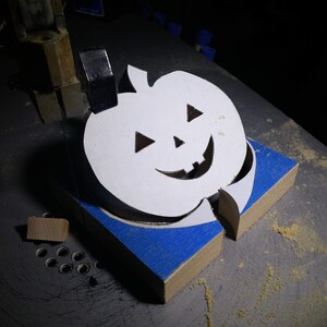 Handmade unpainted wooden Jack-o-Lantern cutout with carved triangular eyes, nose, smiling mouth, and stem, shown freestanding on a white background.Finished cutting on myscroll saw.
