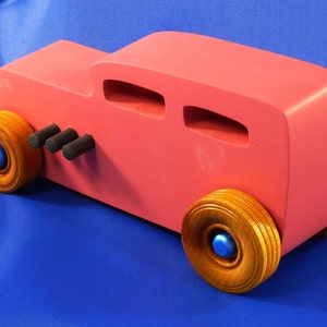 Handcrafted pink wooden hot rod '32 sedan toy car. Features black and metallic sapphire blue accents, and non-marking amber shellac wheels. Made to order for unique play or display.