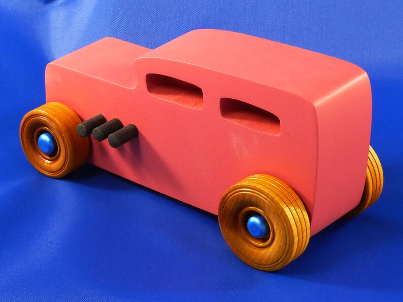 Handcrafted pink wooden hot rod '32 sedan toy car. Features black and metallic sapphire blue accents, and non-marking amber shellac wheels. Made to order for unique play or display.