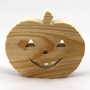 Handmade unpainted wooden Jack-o-Lantern cutout with carved triangular eyes, nose, smiling mouth, and stem, shown freestanding on a white background. Ready to paint for Halloween decoration.