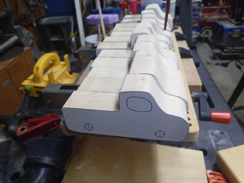 A row of unfinished wooden toy pickup bodies on a workshop bench, with paper patterns showing the cab windows and wheel positions.