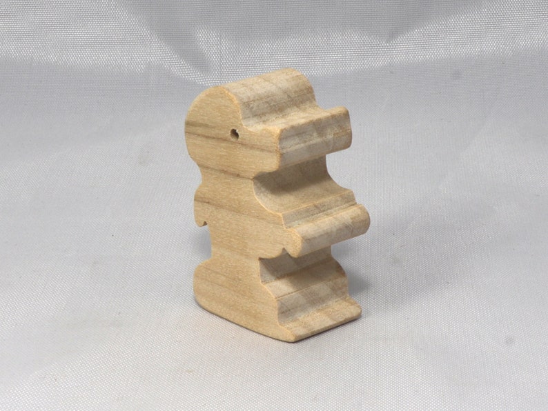 May include: A wooden toy shaped like a person, standing upright with arms outstretched. The toy is made of light brown wood and has a simple, minimalist design.
