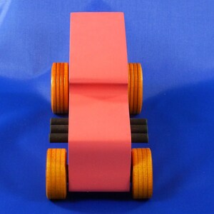 Handcrafted pink wooden hot rod '32 sedan toy car. Features black and metallic sapphire blue accents, and non-marking amber shellac wheels. Made to order for unique play or display.