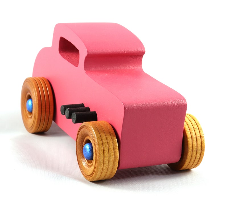 This is a handmade wooden Hot Rod '32 Deuce Coupe toy car. It is hand-painted hot pink with black and metallic sapphire blue trim. The hardwood wheels are finished with nonmarring amber shellac.