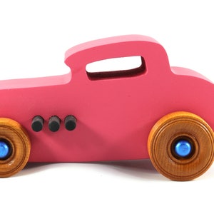This is a handmade wooden Hot Rod '32 Deuce Coupe toy car. It is hand-painted hot pink with black and metallic sapphire blue trim. The hardwood wheels are finished with nonmarring amber shellac.