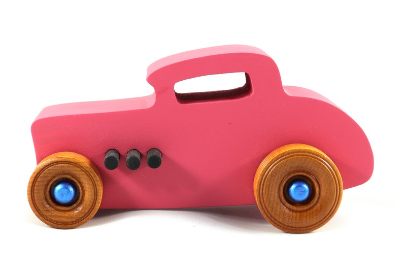 This is a handmade wooden Hot Rod '32 Deuce Coupe toy car. It is hand-painted hot pink with black and metallic sapphire blue trim. The hardwood wheels are finished with nonmarring amber shellac.
