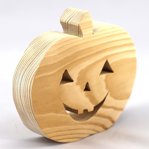 Handmade unpainted wooden Jack-o-Lantern cutout with carved triangular eyes, nose, smiling mouth, and stem, shown freestanding on a white background. Ready to paint for Halloween decoration.