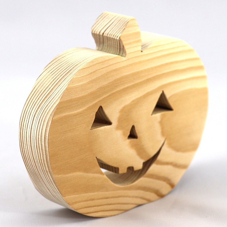 Handmade unpainted wooden Jack-o-Lantern cutout with carved triangular eyes, nose, smiling mouth, and stem, shown freestanding on a white background. Ready to paint for Halloween decoration.