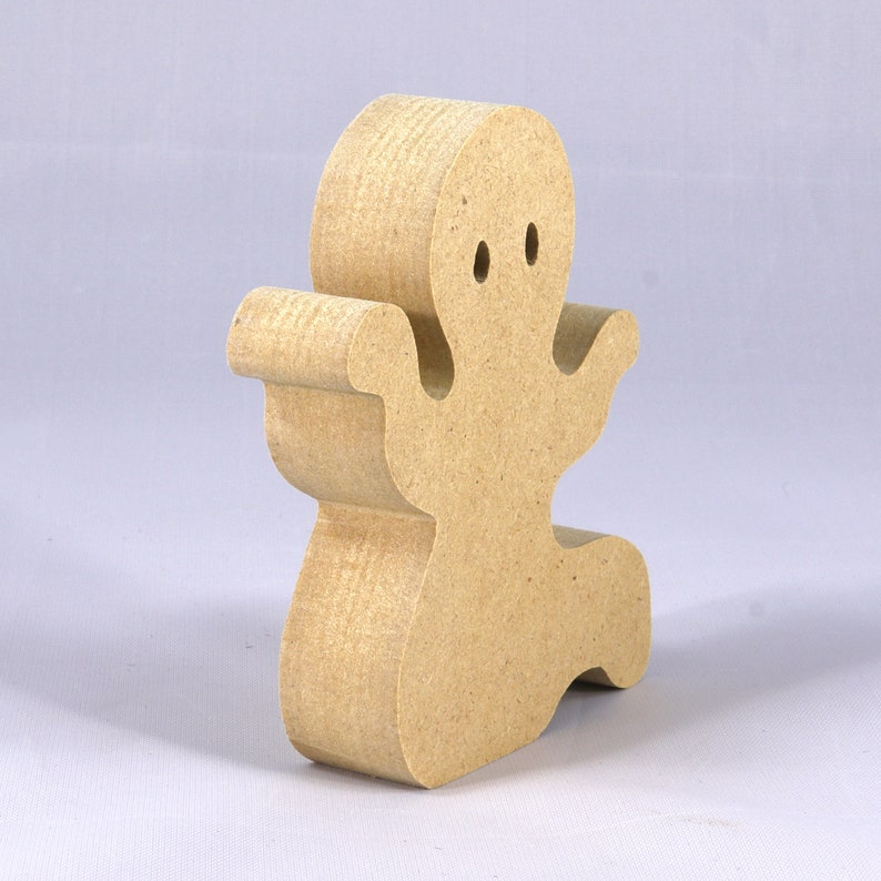 A handmade, unpainted wooden ghost cutout stands upright on a white background. The light-colored solid wood figure has a rounded head with two circular eye cutouts, raised wavy arms, and a curved wavy base, ready for painting or crafting.
