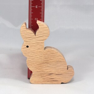 May include: A wooden rabbit figurine, approximately 3 inches tall, with a light brown color and a smooth, slightly textured surface.