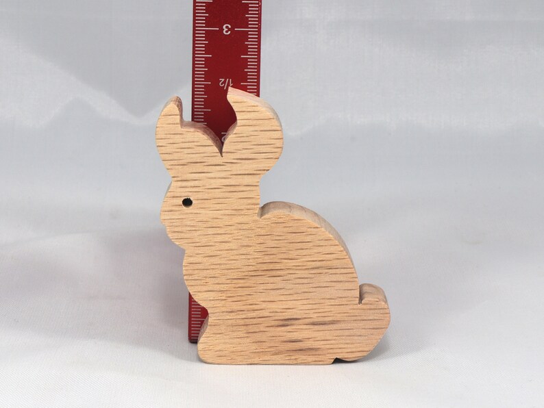 May include: A wooden rabbit figurine, approximately 3 inches tall, with a light brown color and a smooth, slightly textured surface.