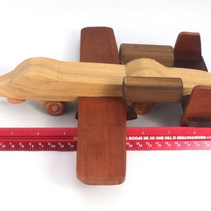 May include: A handcrafted wooden toy airplane with a light brown body, dark brown wings, and wheels. The toy is approximately 10 inches long and is set against a white background.
