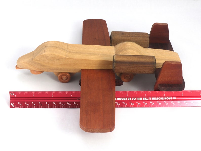 May include: A handcrafted wooden toy airplane with a light brown body, dark brown wings, and wheels. The toy is approximately 10 inches long and is set against a white background.
