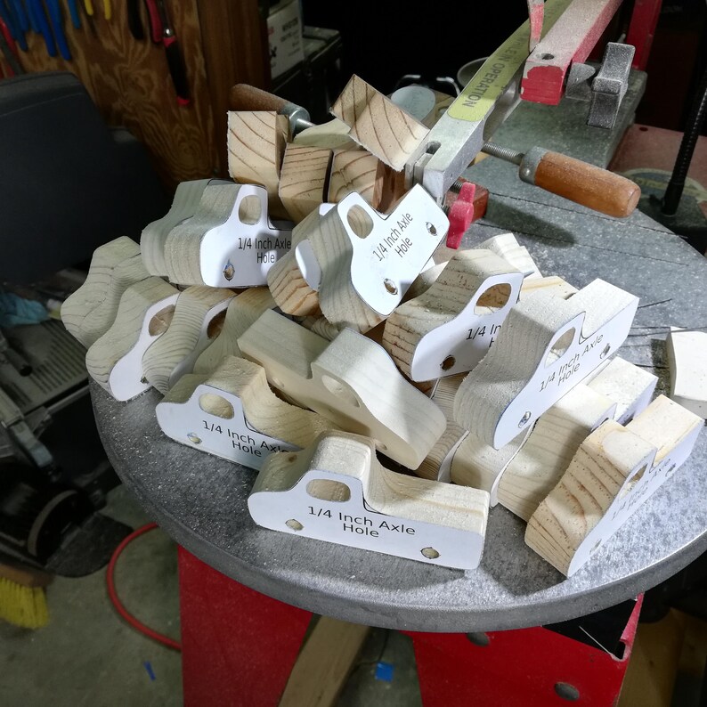Handmade wooden toy pickup truck bodies stacked on a scroll saw table during construction, with patterns marking the axle holes.