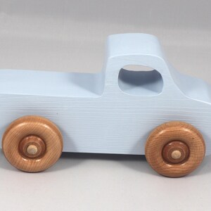 May include: A light blue wooden toy truck with natural wood wheels. The truck has a classic pickup design with a cab and a cargo bed. The wheels are round and attached to the truck's body. A charming, handcrafted toy.