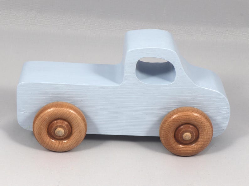 May include: A light blue wooden toy truck with natural wood wheels. The truck has a classic pickup design with a cab and a cargo bed. The wheels are round and attached to the truck's body. A charming, handcrafted toy.