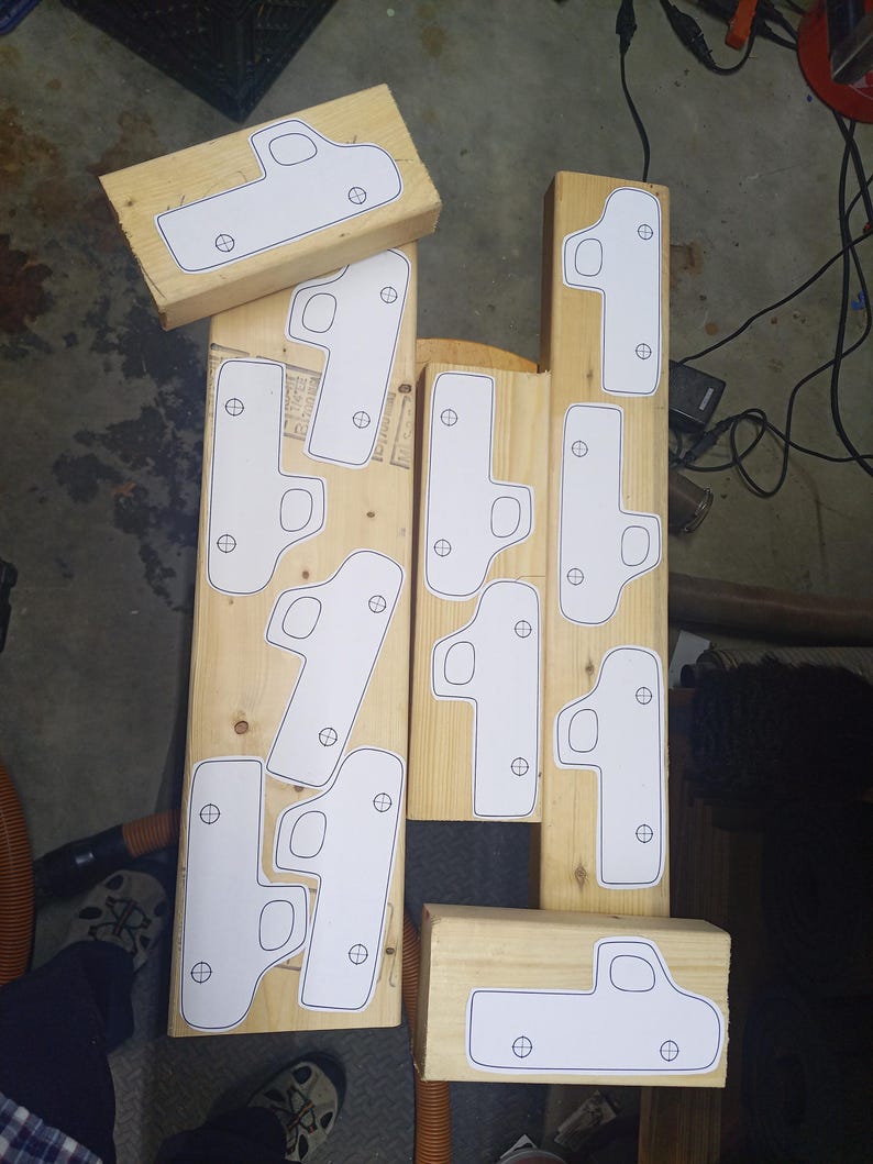 Overhead view of paper toy pickup truck patterns arranged on pine boards, with cab windows and axle holes marked for cutting.