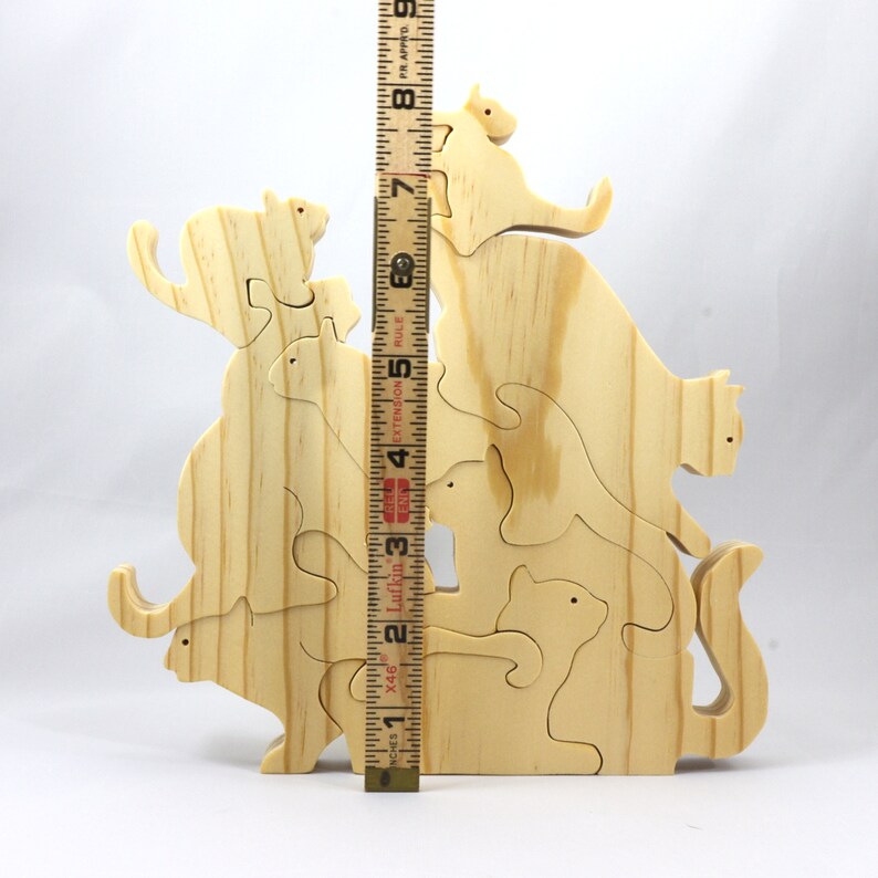 Handmade wooden puzzle featuring several cat-shaped pieces stacked on top of each other in various playful poses, forming a balanced tower. The cats are crafted with smooth edges and natural wood tones, highlighting their unique shapes and expressions.