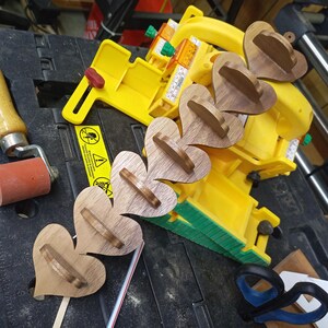 This handmade wooden heart shelf, crafted from walnut, rests on my work table among a variety of tools. It features seven shelves, perfect for displaying small treasures.