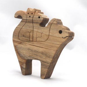 A freestanding wooden puzzle cut in the shape of a large cat standing on four legs. Two smaller kitten figures nest on the large cat’s back and interlock as puzzle pieces. Simple drilled holes form the eyes and nose on each cat, with a shallow cut line for the mouth on the large cat. The completed puzzle stands upright on a plain white surface. Handmade by Odin’s Toy Factory In Tallahassee, Florida, USA.