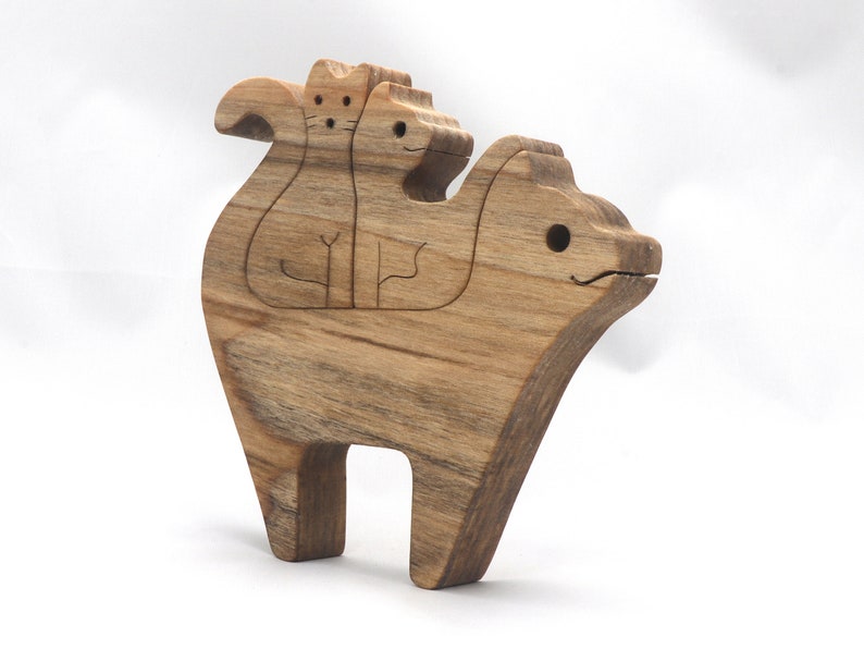 A freestanding wooden puzzle cut in the shape of a large cat standing on four legs. Two smaller kitten figures nest on the large cat’s back and interlock as puzzle pieces. Simple drilled holes form the eyes and nose on each cat, with a shallow cut line for the mouth on the large cat. The completed puzzle stands upright on a plain white surface. Handmade by Odin’s Toy Factory In Tallahassee, Florida, USA.