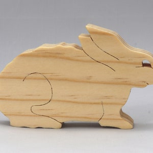 May include: A wooden rabbit cutout, made of light brown wood with a smooth, unfinished surface. The rabbit is in a sitting position with its ears perked up.
