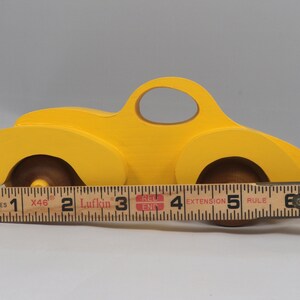 Handmade wooden toy car vintage style of a fat fendered coupe painted bright yellow with nonmarring amber shellac finished wheels. It is an excellent push toy for a younger child.