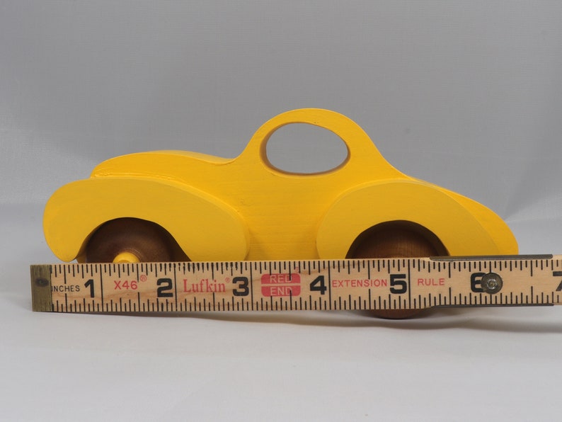 Handmade wooden toy car vintage style of a fat fendered coupe painted bright yellow with nonmarring amber shellac finished wheels. It is an excellent push toy for a younger child.