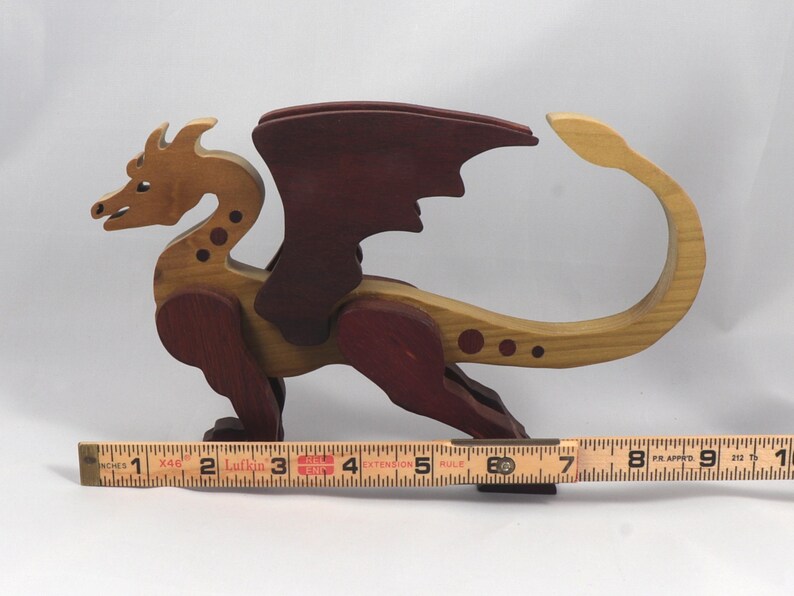 Handmade wooden dragon figurine made from contrasting hardwoods with a light natural wood body and head paired with rich dark reddish-brown wings, legs, and horns. Displayed with a wooden carpenters rule for scale.