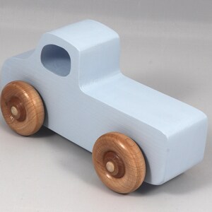 May include: A light blue wooden toy truck with natural wood wheels. The truck has a simple, blocky design with a cab and a cargo bed. The wheels are round and attached to the truck's body.
