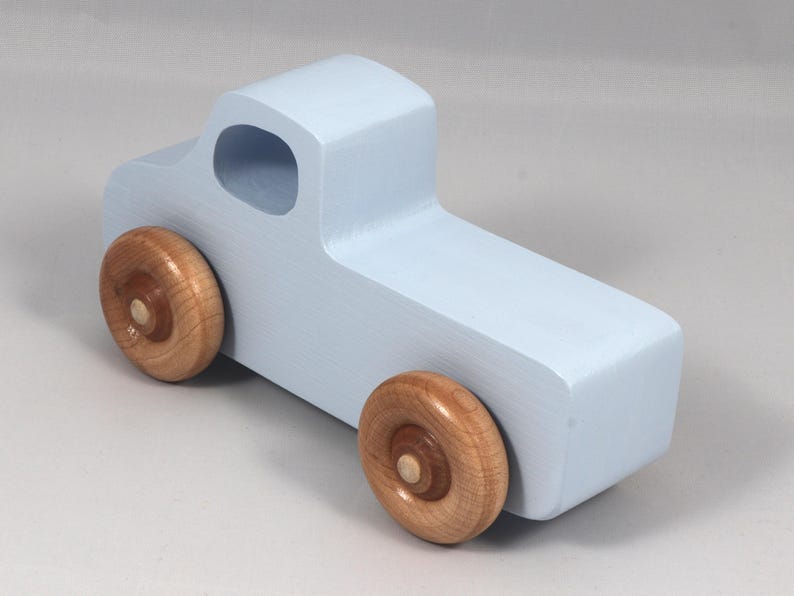 May include: A light blue wooden toy truck with natural wood wheels. The truck has a simple, blocky design with a cab and a cargo bed. The wheels are round and attached to the truck's body.