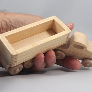 May include: A wooden toy truck with a removable bed. The truck is made of unfinished wood and has four wheels. The bed is empty and ready to be filled with toys or other items.