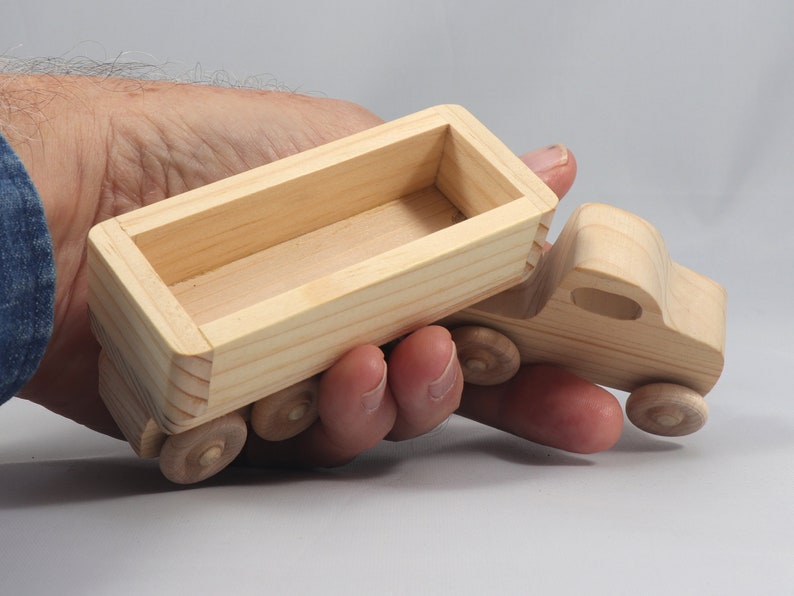 May include: A wooden toy truck with a removable bed. The truck is made of unfinished wood and has four wheels. The bed is empty and ready to be filled with toys or other items.