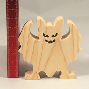 Handmade unpainted wooden Halloween bat cutout, freestanding light-colored solid wood figure with spooky carved face and outstretched wings, ready to paint, from my Snazzy Spooks collection. Standing beside a ruler.