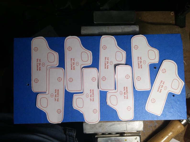 Paper pickup truck patterns arranged on blue-taped wood, ready for cutting into handmade wooden toy trucks.