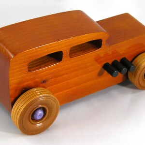 This is a handmade wooden toy car modeled after a Hot Rod 1932 Ford Sedan. It is made from wood, finished with multiple coats of amber shellac, and trimmed with black and metallic purple acrylic paint.