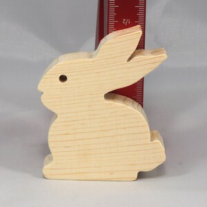 May include: A wooden rabbit cutout, approximately 4 inches tall, made of unfinished light wood. The rabbit is standing on a white surface.