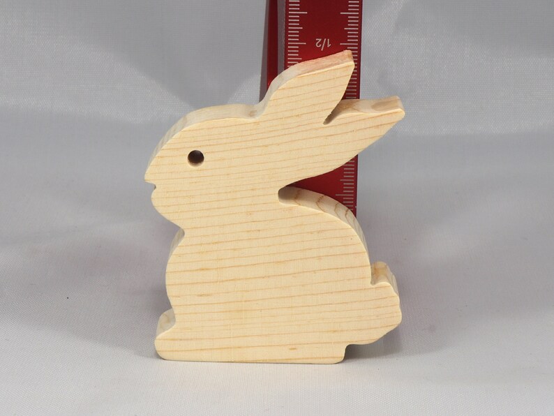 May include: A wooden rabbit cutout, approximately 4 inches tall, made of unfinished light wood. The rabbit is standing on a white surface.