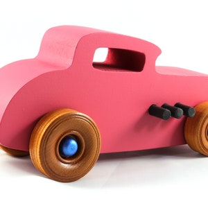 This is a handmade wooden Hot Rod '32 Deuce Coupe toy car. It is hand-painted hot pink with black and metallic sapphire blue trim. The hardwood wheels are finished with nonmarring amber shellac.