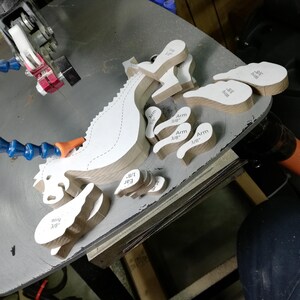 Freshly scroll-sawn wooden baby dragon body, wings, arms, legs, and ears arranged on the saw table before sanding and assembly.