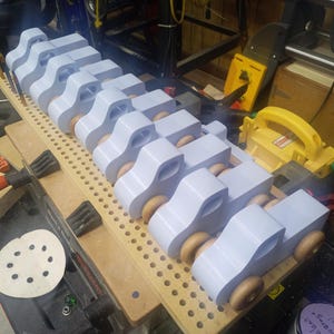 A row of pale blue wooden toy pickup trucks with amber-finished wheels lined up on a perforated board in the workshop.